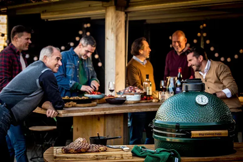 Friends gathered around a Big Green Egg, sharing food and conversation